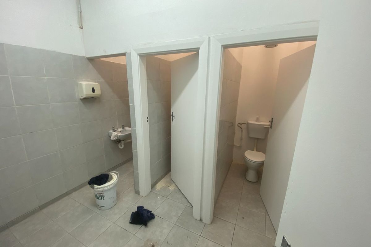 A functional industrial bathroom facility featuring tiled walls and floors, a wall-mounted basin, and separate toilet cubicles.