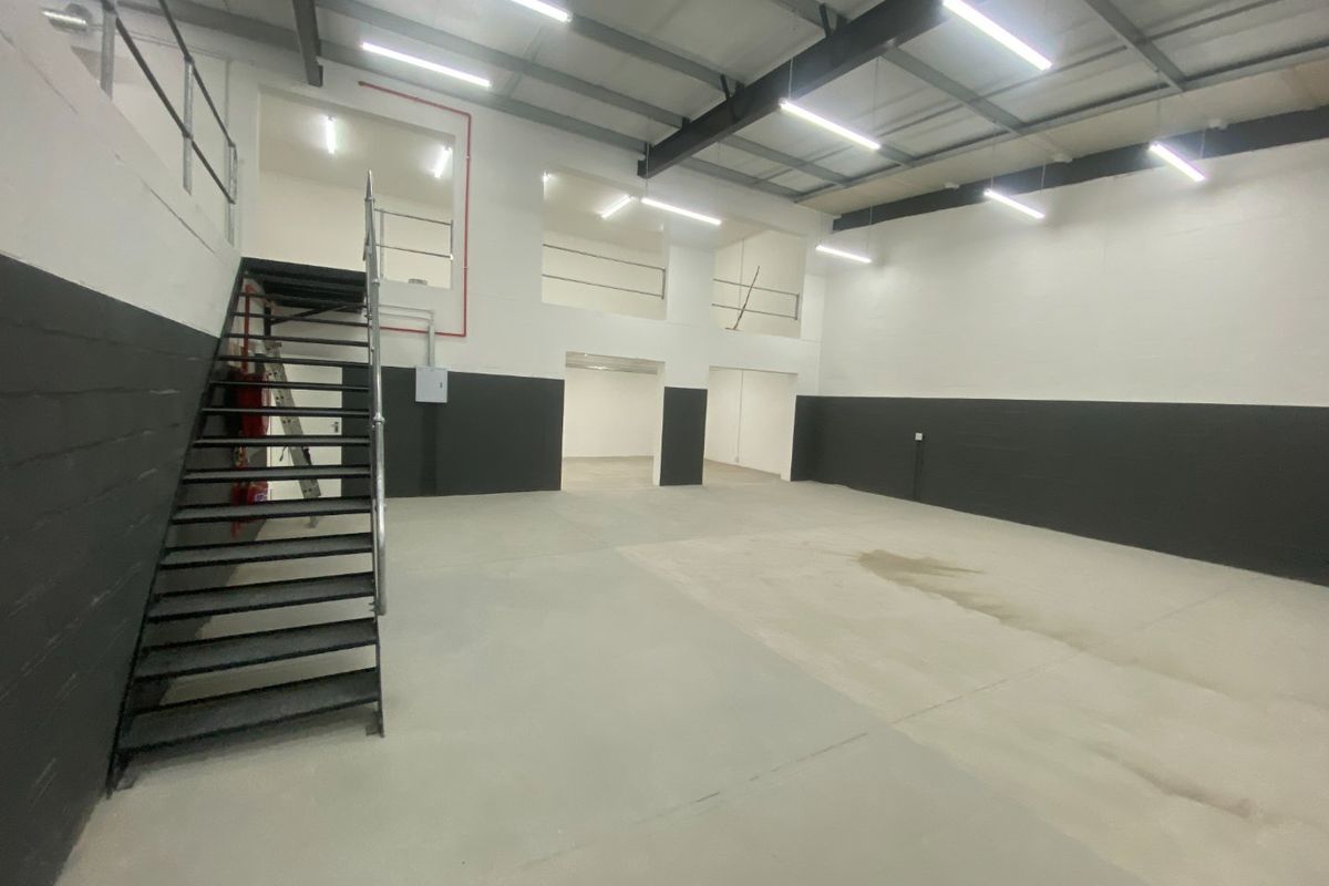 Spacious industrial utility area featuring high ceilings, exposed steel beams, concrete flooring, and a metal staircase leading to a mezzanine level.