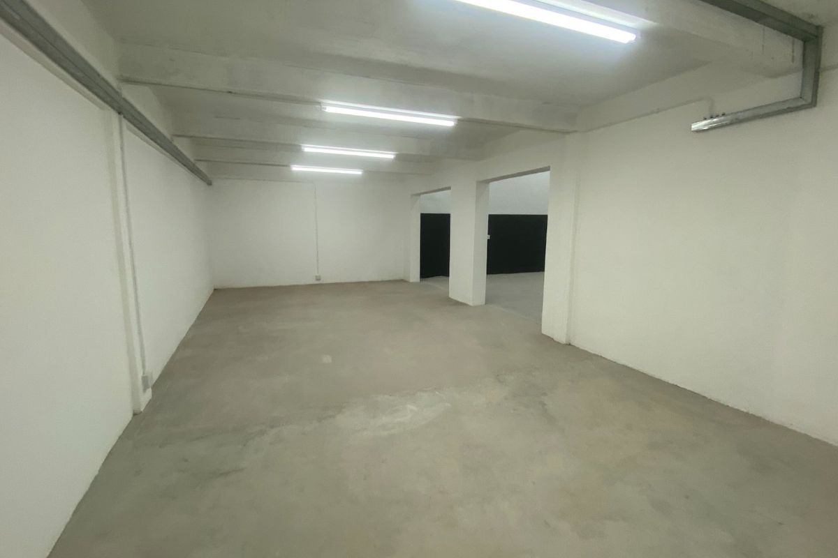 A spacious, empty industrial utility area featuring exposed concrete ceilings, fluorescent lighting, and concrete flooring, suitable for storage or workshop use.