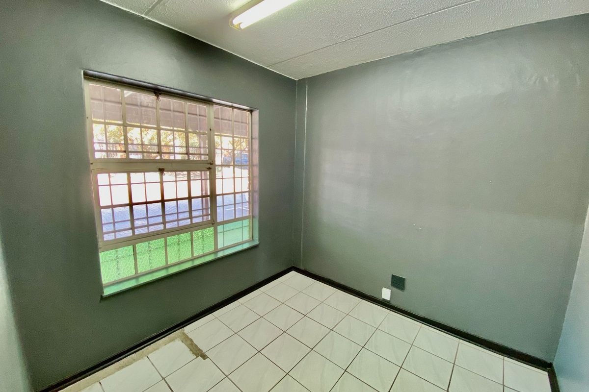 An empty office space featuring tiled flooring, security bars on the window, and fluorescent lighting, suitable for a professional workspace.