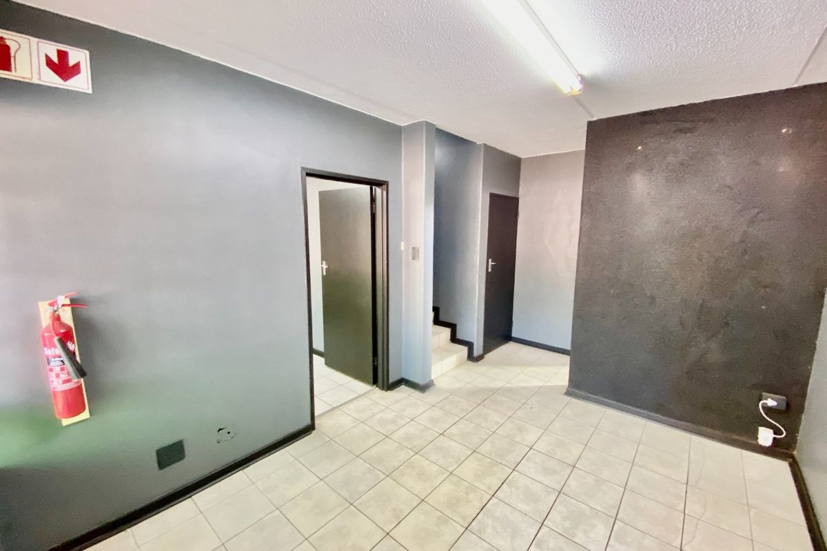 A functional industrial hallway featuring tiled flooring, fluorescent lighting, and access to multiple rooms and a staircase.