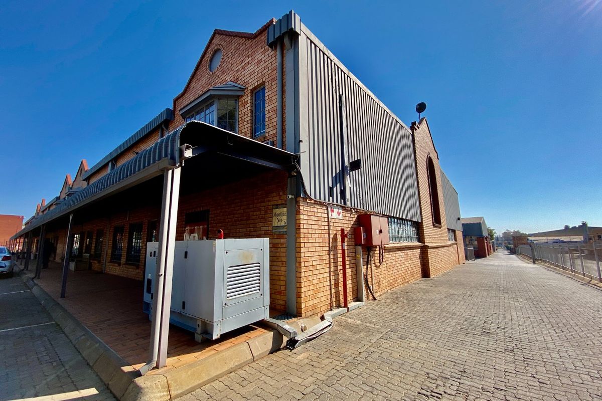Exterior view of an industrial building featuring brick and metal cladding, a paved driveway, and a covered walkway with an external generator.