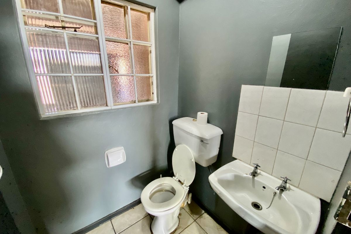 A functional bathroom featuring a wall-mounted basin with tiled splashback, ceramic toilet, and a window with textured glass.