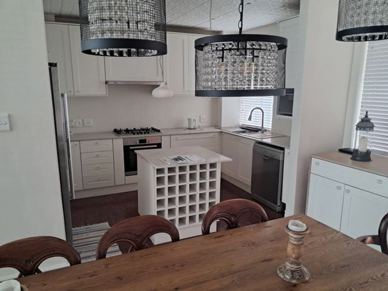 Open plan kitchen featuring white cabinetry, gas hob, built-in oven, and a central wine rack island, seamlessly flowing into the dining area.