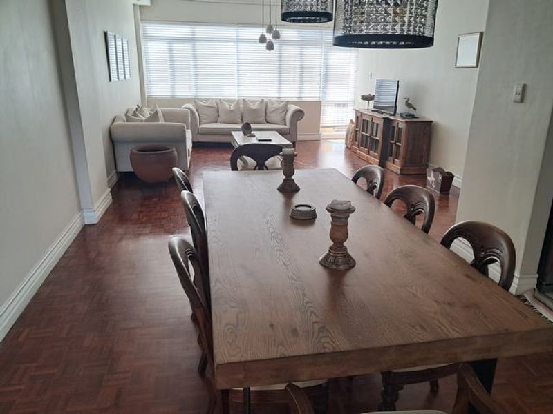 Spacious open-plan living and dining area featuring classic parquet flooring, large windows with venetian blinds, and decorative pendant lighting.