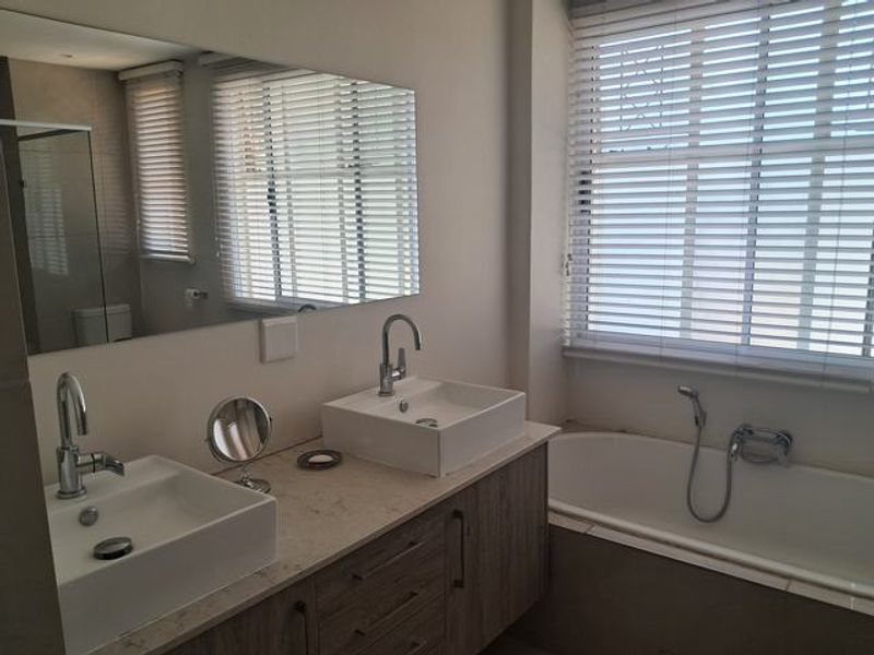 Modern bathroom featuring a double vanity with vessel sinks, stone countertop, and a built-in bathtub with a handheld shower attachment.