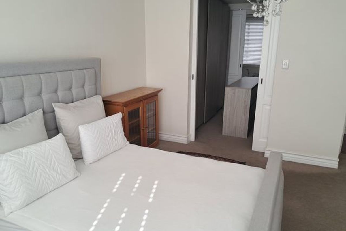 A well-maintained bedroom featuring neutral carpeting, built-in cupboards, and a sliding door leading to an adjacent dressing or utility area.