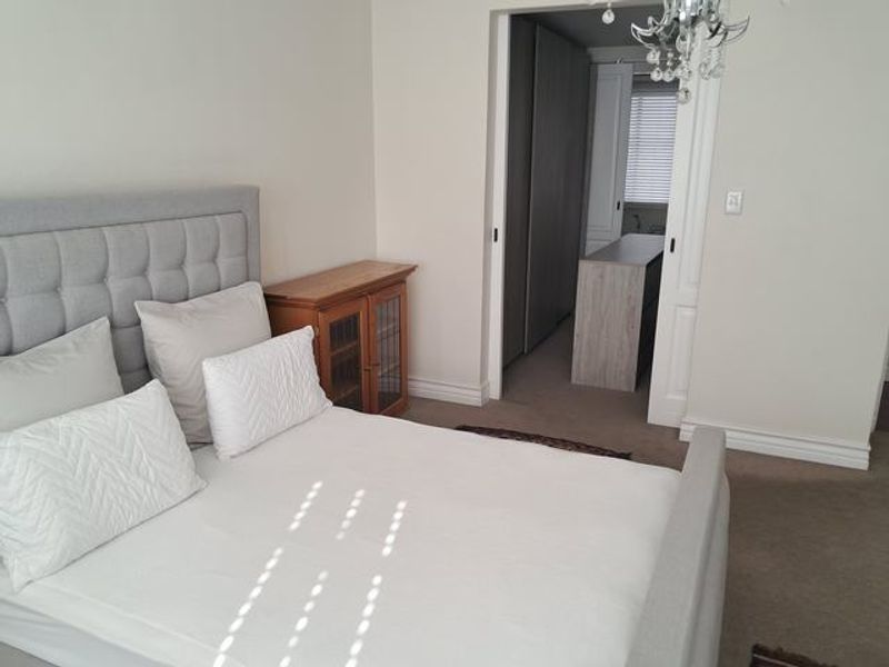 A well-maintained bedroom featuring neutral carpeting, built-in cupboards, and a sliding door leading to an adjacent dressing or utility area.