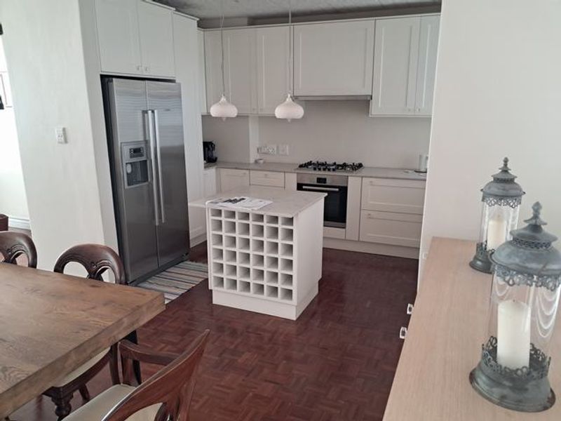 Modern kitchen featuring white shaker-style cabinetry, a central island with integrated wine storage, gas hob, and classic parquet flooring.
