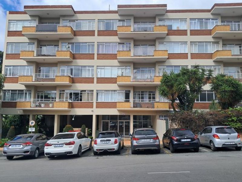 Front elevation of a multi-story apartment building featuring brick facade, private balconies for each unit, and ground-level parking.