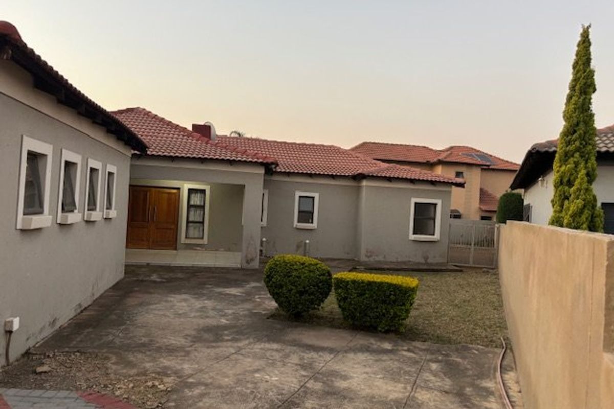 Rear exterior view of the house featuring a tiled roof, concrete paved area, and a boundary wall with established garden shrubs.