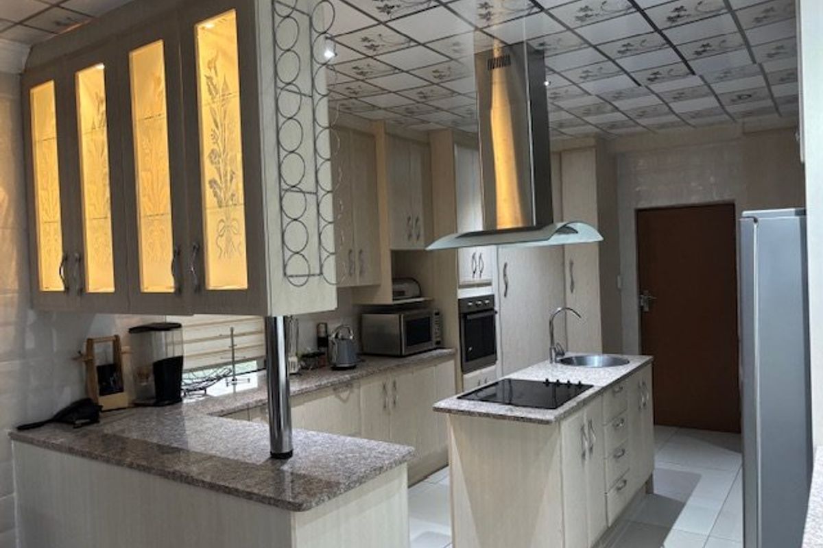 A functional kitchen featuring granite countertops, built-in cabinetry, a central island with a hob, and a stainless steel extractor fan.