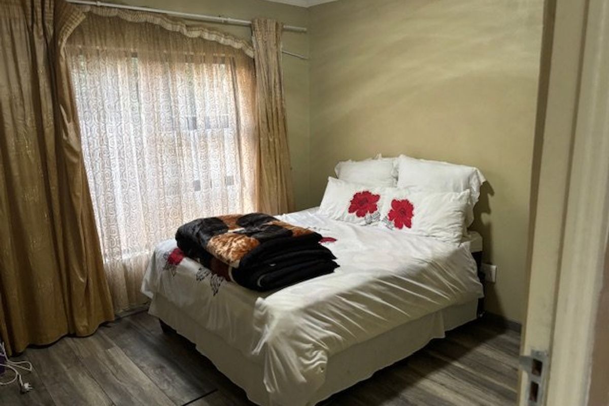 A standard bedroom featuring laminate flooring, neutral wall finishes, and large window with curtain rails.