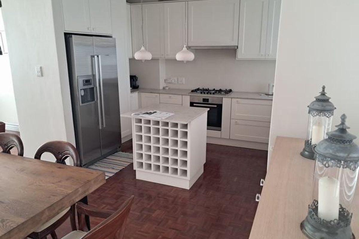 Modern kitchen featuring white shaker-style cabinetry, a central island with integrated wine storage, gas hob, and classic parquet flooring.