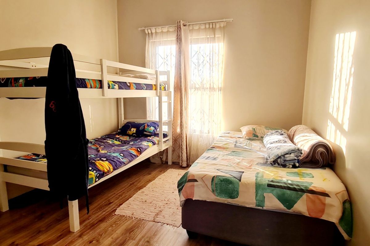 A functional bedroom featuring laminate flooring, natural light through a window with security gate, and space for multiple beds.