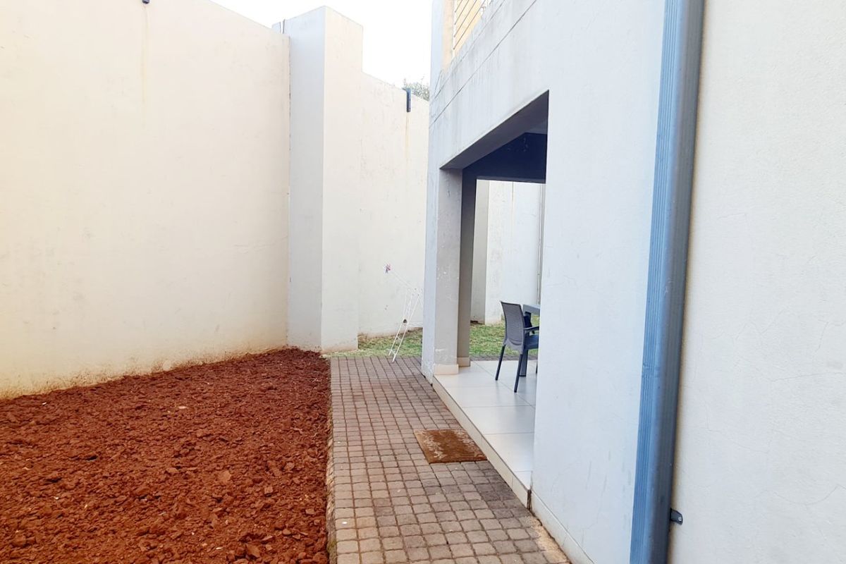 Rear exterior area featuring a paved walkway, covered patio space, and high boundary walls, requiring landscaping and maintenance.