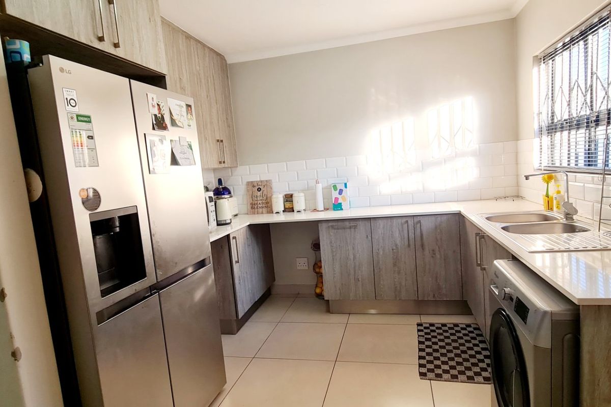 Modern kitchen featuring light wood-grain cabinetry, white subway tile backsplash, quartz countertops, and a double basin sink with security bars on the window.