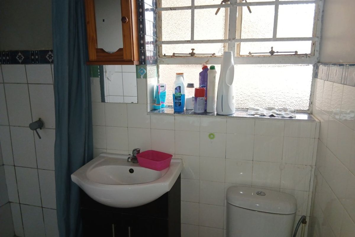 A dated bathroom featuring a vanity basin, toilet, and tiled walls with a window, requiring cosmetic updates to improve its overall condition.