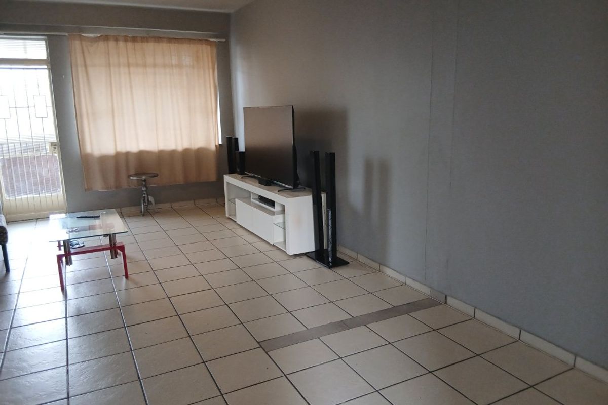 A spacious living room featuring neutral tiled flooring and a sliding glass door with an integrated security gate leading to an outdoor area.