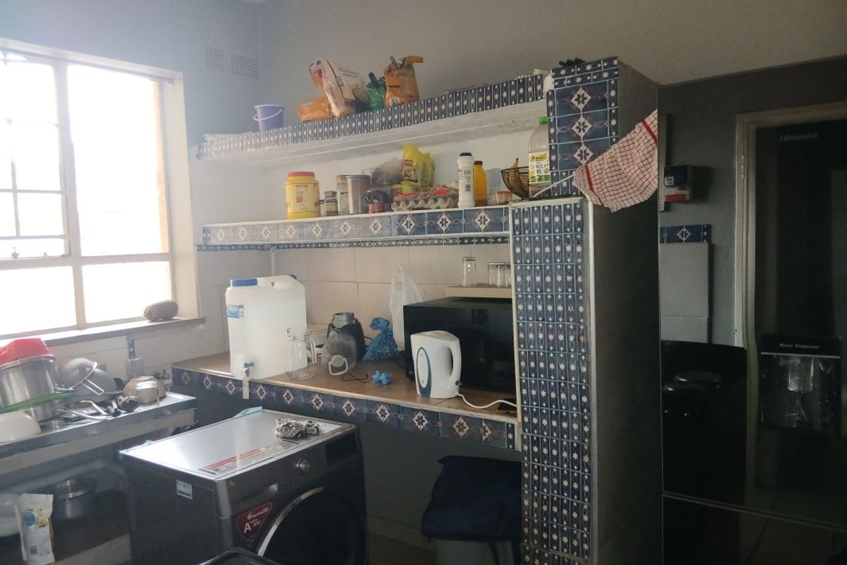 A functional kitchen area featuring tiled countertops, built-in shelving, and a tiled splashback, offering a practical layout for daily food preparation and laundry tasks.