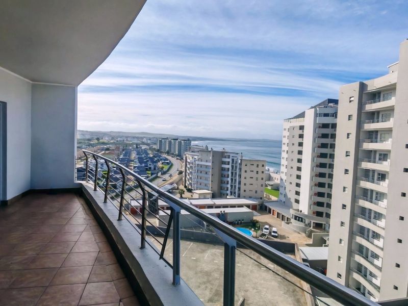 Spacious covered balcony featuring tiled flooring and a modern glass balustrade, offering expansive coastal and urban views.