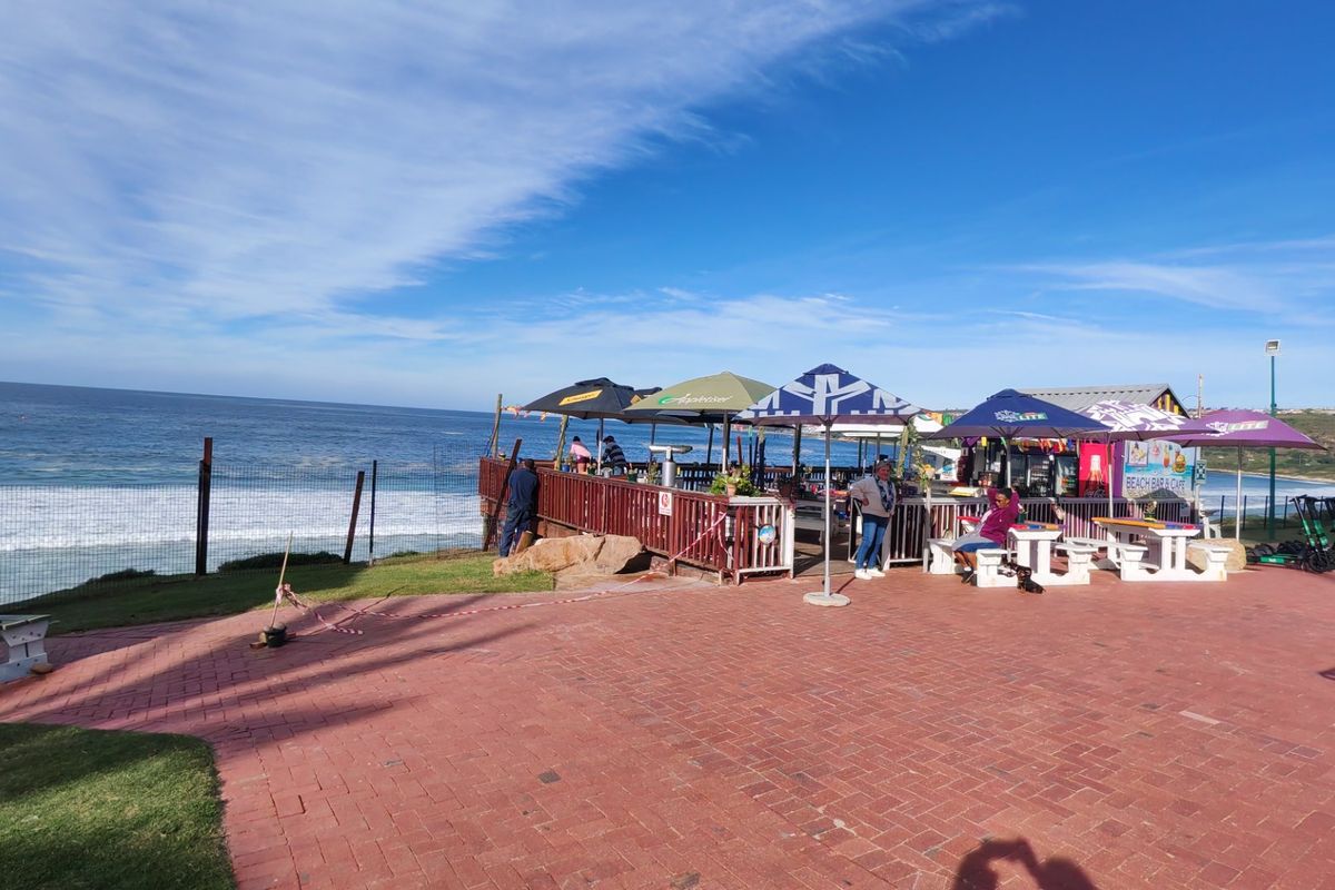 Outdoor paved patio area with a wooden deck overlooking the ocean, featuring perimeter fencing and coastal views.
