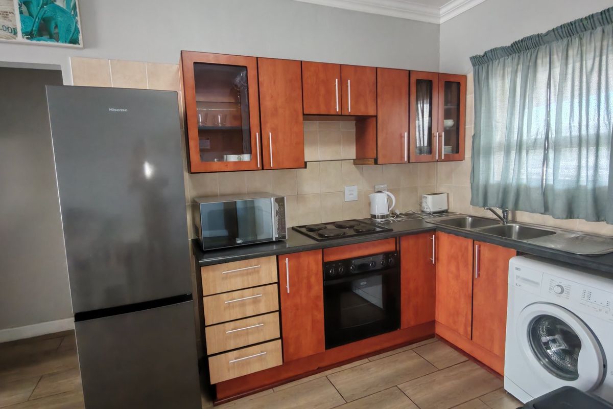 A functional kitchen featuring wood-finish cabinetry, dark countertops, built-in oven and hob, double sink, and tiled flooring with integrated laundry appliance space.