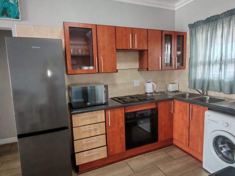 A functional kitchen featuring wood-finish cabinetry, dark countertops, built-in oven and hob, double sink, and tiled flooring with integrated laundry appliance space.