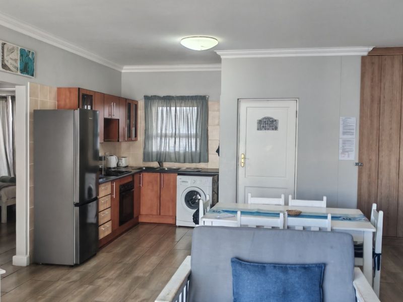 Open plan living area featuring a functional kitchen with built-in cabinetry, oven, hob, and laundry plumbing, finished with laminate flooring and crown molding.