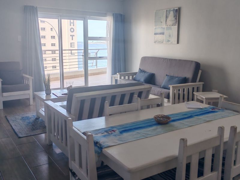 Open plan living and dining area featuring tiled flooring and large sliding glass doors leading to a balcony with coastal views.