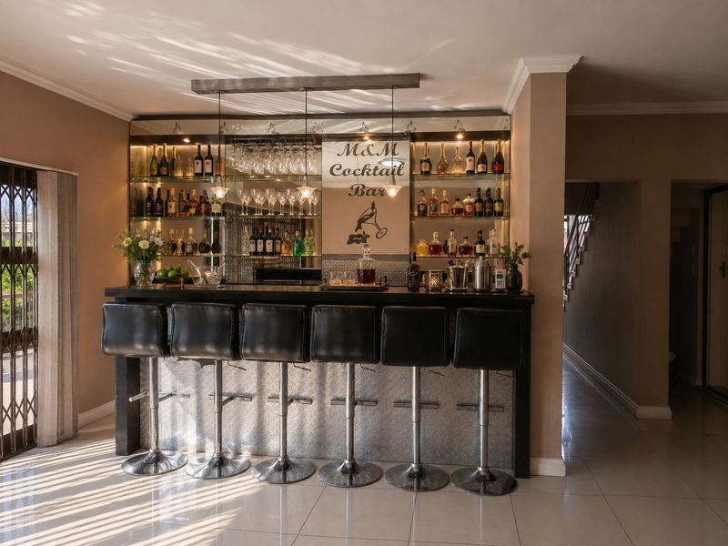 A well-appointed home bar featuring a built-in counter, mirrored back bar with glass shelving, and integrated lighting, perfect for entertaining.