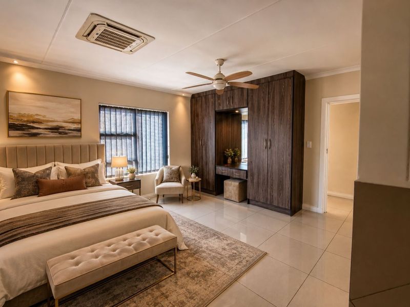 Spacious bedroom featuring modern built-in cupboards with an integrated vanity, tiled flooring, ceiling fan, and a recessed air conditioning unit.
