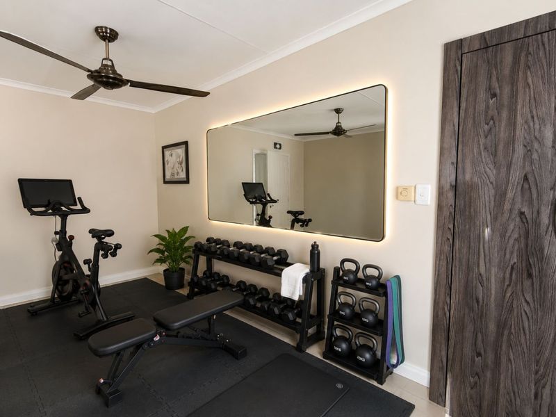 A well-maintained home gym featuring a large backlit wall mirror, ceiling fan, and modern timber-look door, providing a clean and functional workout space.