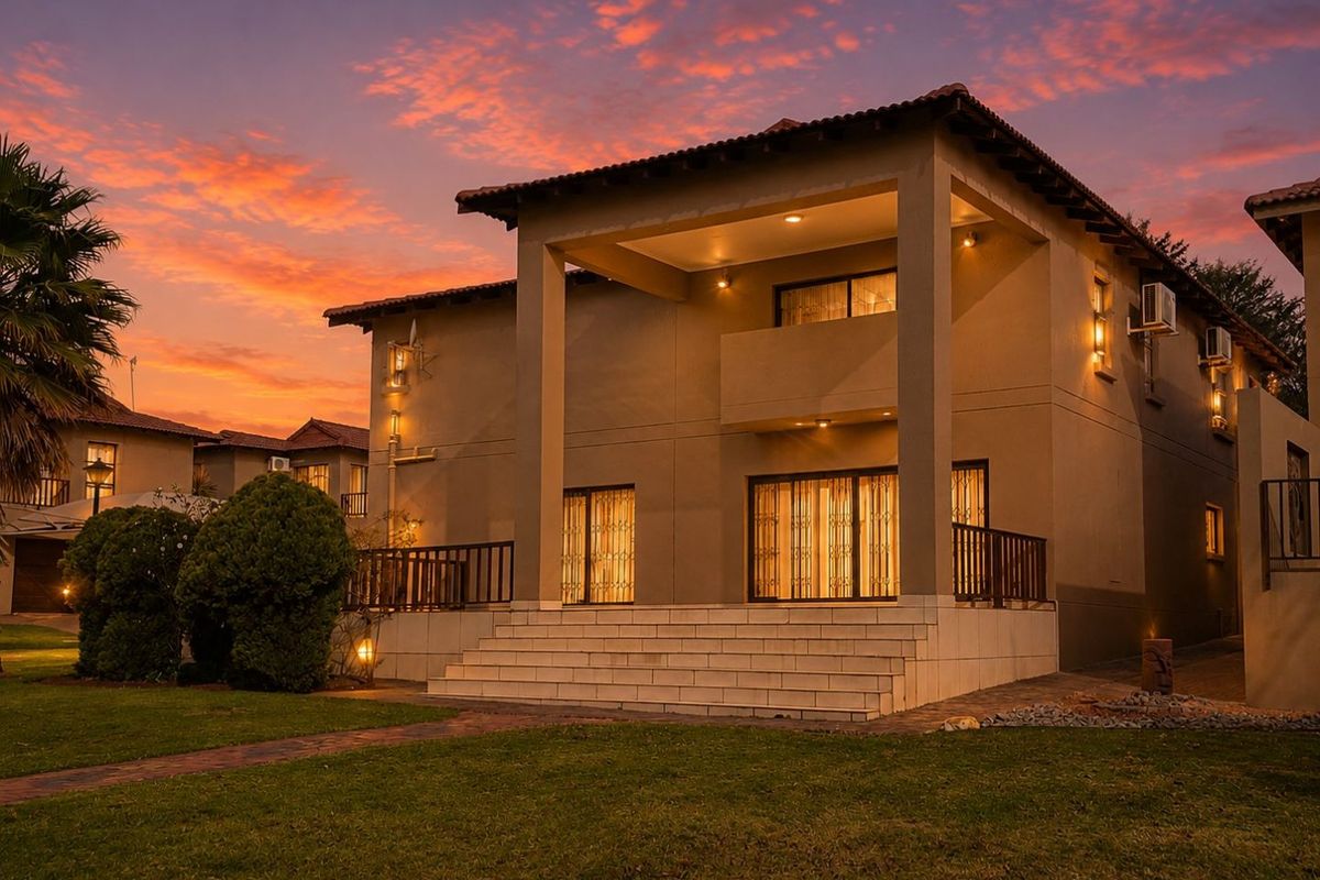 A well-maintained double-story residence featuring a covered patio, balcony, and landscaped garden, captured during a vibrant sunset.