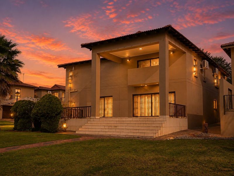 A well-maintained double-story residence featuring a covered patio, balcony, and landscaped garden, captured during a vibrant sunset.