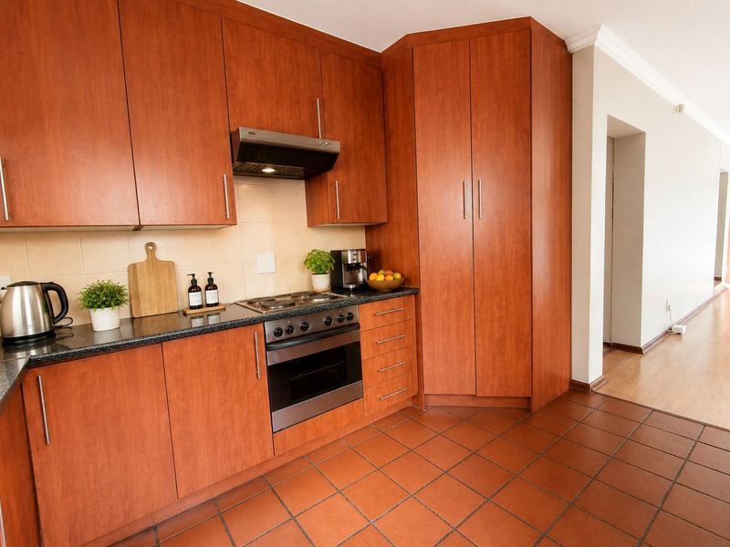 A functional kitchen featuring warm-toned wood cabinetry, dark laminate countertops, a built-in oven with hob, and durable terracotta-style floor tiles.