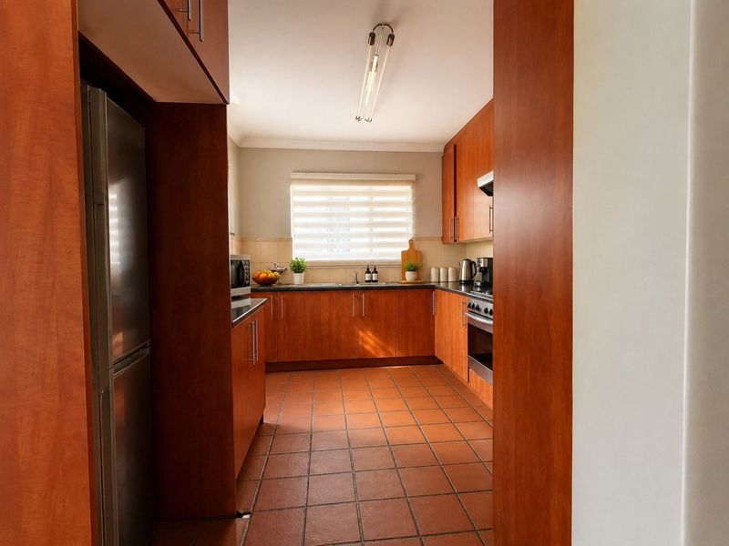 A functional kitchen featuring warm-toned wooden cabinetry, dark countertops, tiled flooring, and integrated appliances, offering a practical layout for daily cooking.