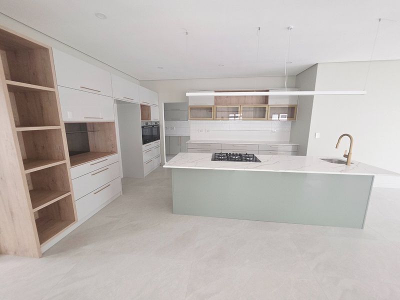 A modern, high-end kitchen featuring a large island with a gas hob, stone countertops, integrated cabinetry, and premium brass fixtures in a bright, open space.