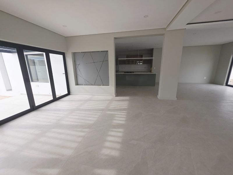 Spacious open-plan living area featuring large sliding glass doors, neutral tiled flooring, and a modern kitchen with a central island and built-in cabinetry.