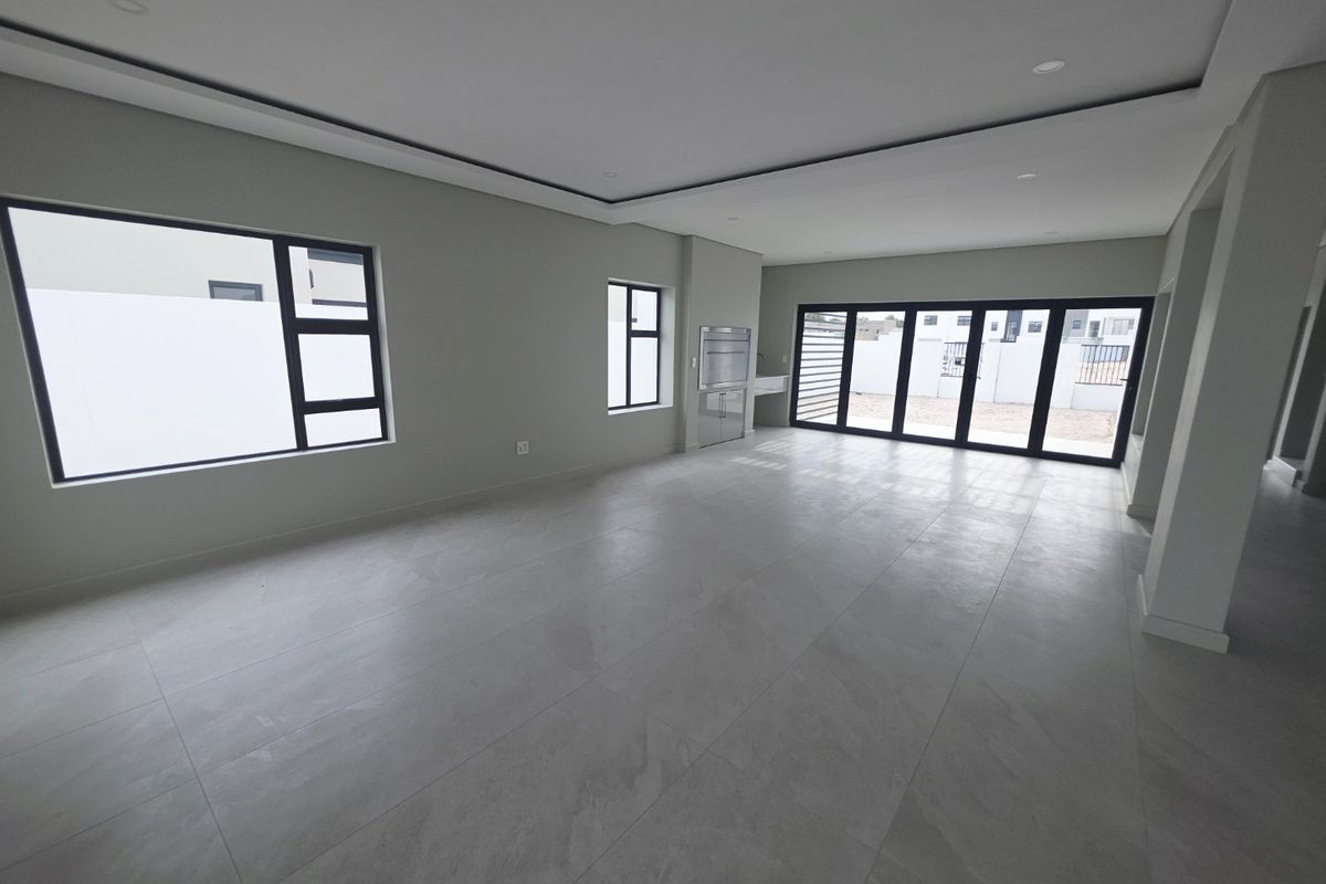 Spacious open-plan living area featuring modern tiled flooring, recessed ceiling details, built-in braai, and large aluminium sliding doors leading to the exterior.