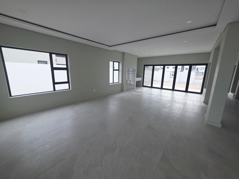 Spacious open-plan living area featuring modern tiled flooring, recessed ceiling details, built-in braai, and large aluminium sliding doors leading to the exterior.