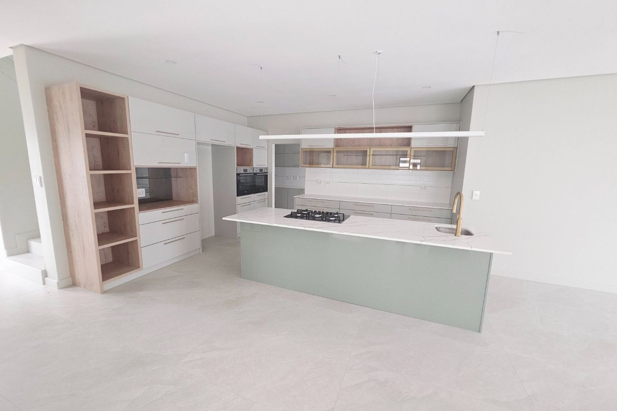Modern, newly installed kitchen featuring a central island with a gas hob, stone countertops, integrated cabinetry, and high-end finishes in a bright, open space.