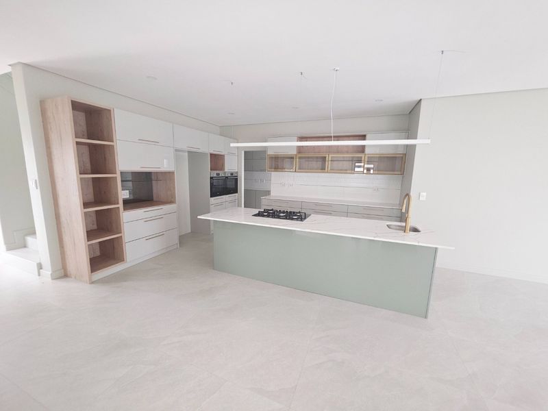 Modern, newly installed kitchen featuring a central island with a gas hob, stone countertops, integrated cabinetry, and high-end finishes in a bright, open space.