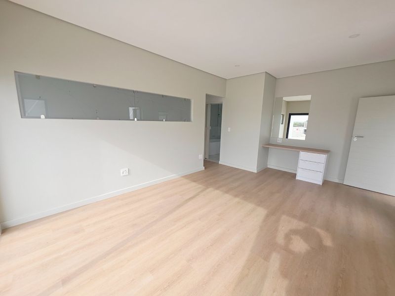 A bright, modern bedroom featuring light laminate flooring, a built-in vanity unit, and neutral wall finishes, offering a clean and contemporary living space.