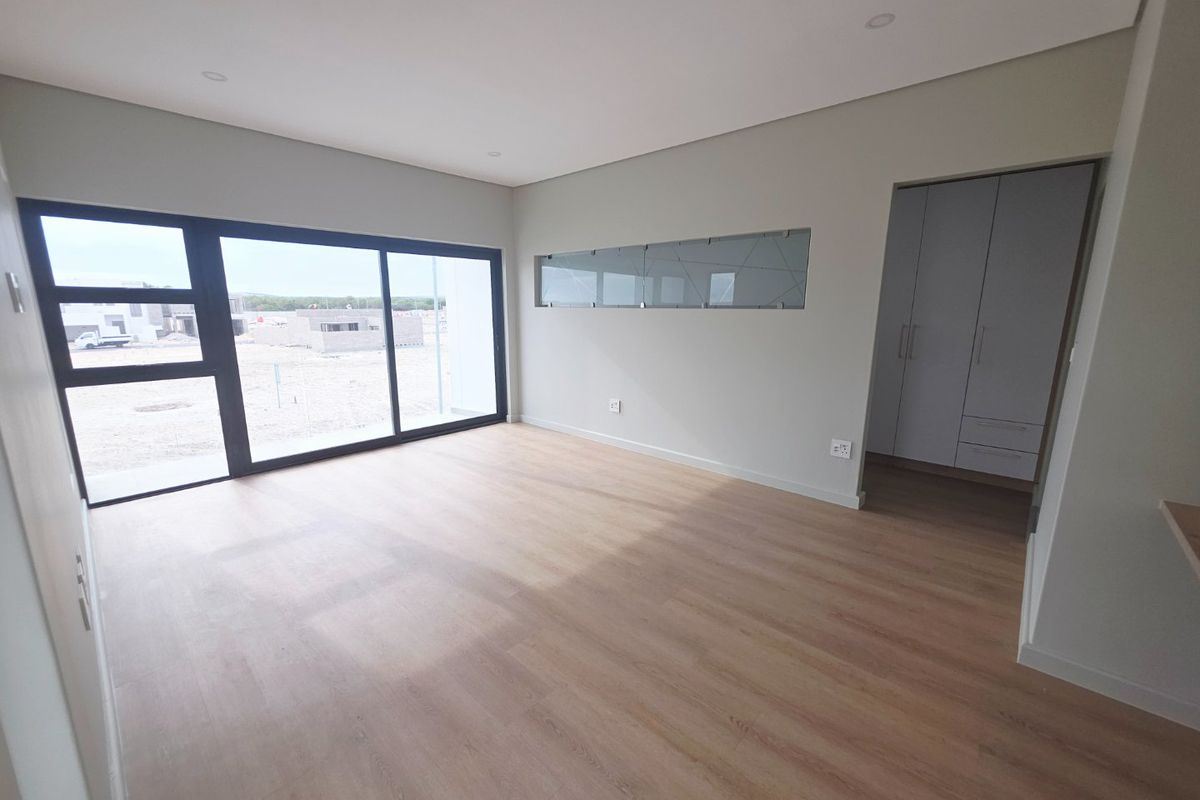 A bright, modern, empty bedroom featuring laminate flooring, recessed lighting, a large sliding glass door, and built-in cupboards with an adjacent dressing area.
