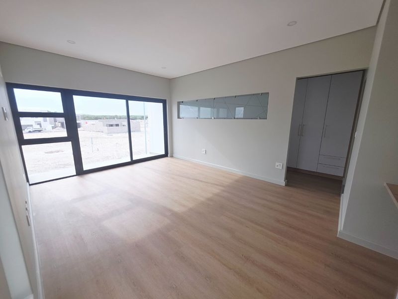 A bright, modern, empty bedroom featuring laminate flooring, recessed lighting, a large sliding glass door, and built-in cupboards with an adjacent dressing area.