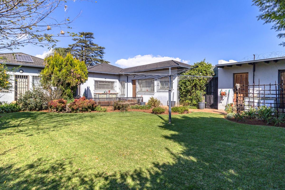 A spacious rear garden featuring a well-maintained lawn, paved patio area, and secure exterior building facade with solar geyser and security features.