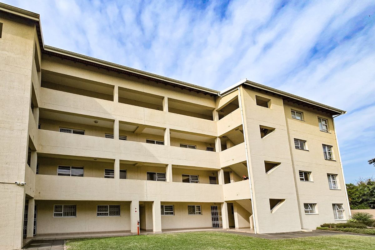Exterior view of a multi-story apartment building featuring private balconies, security gates, and a shared lawn area.