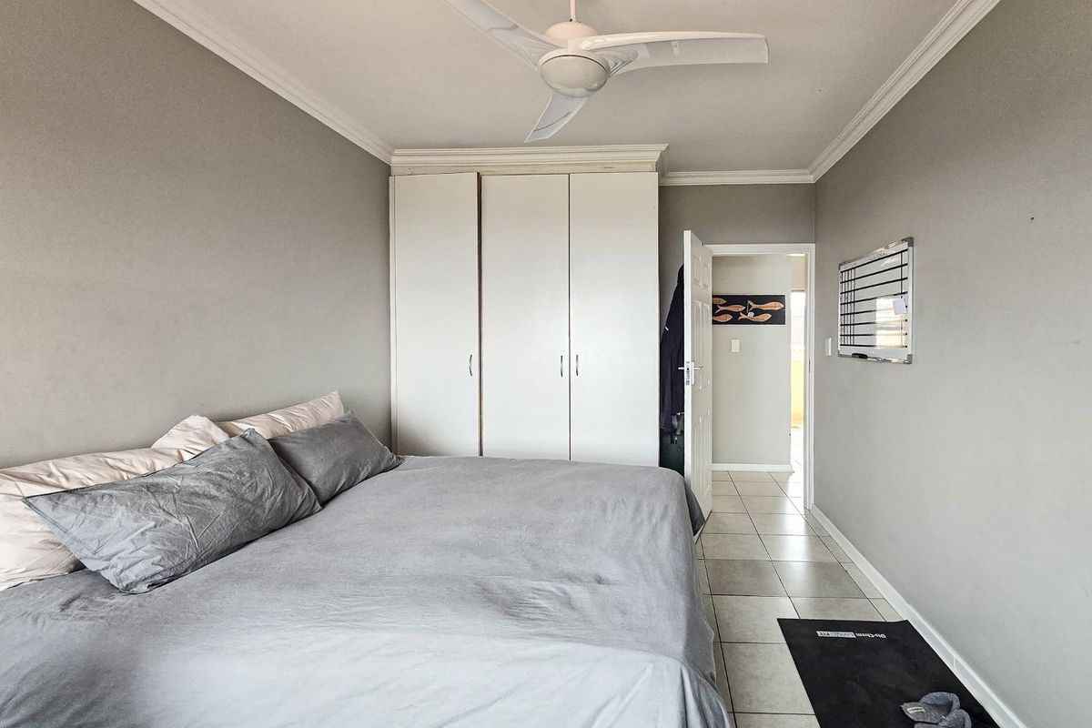 A bedroom featuring tiled flooring, a built-in wardrobe, and a ceiling fan, offering a neutral base for personalization.