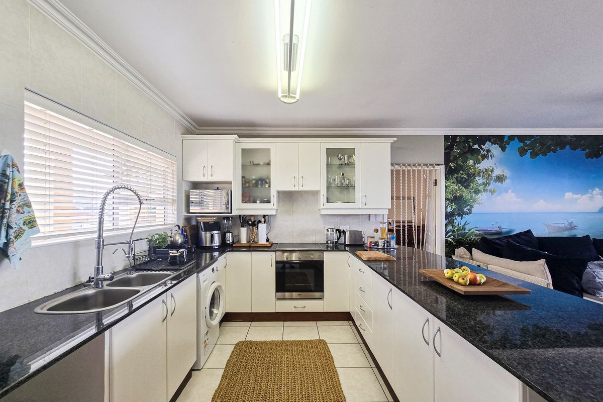 A functional U-shaped kitchen featuring white cabinetry, granite countertops, integrated appliances, and a double basin sink with a modern gooseneck faucet.